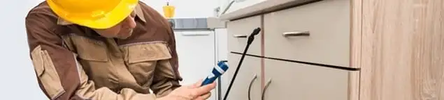 Roach exterminator applying treatment under kitchen cabinets in Phoenix, AZ