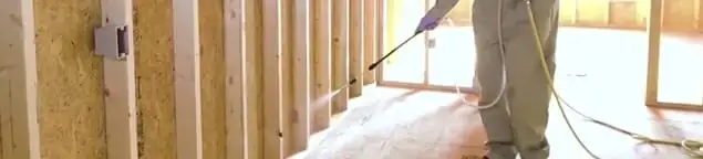 Termite treatment technician applying spray along framing and unfinished walls in Phoenix, AZ
